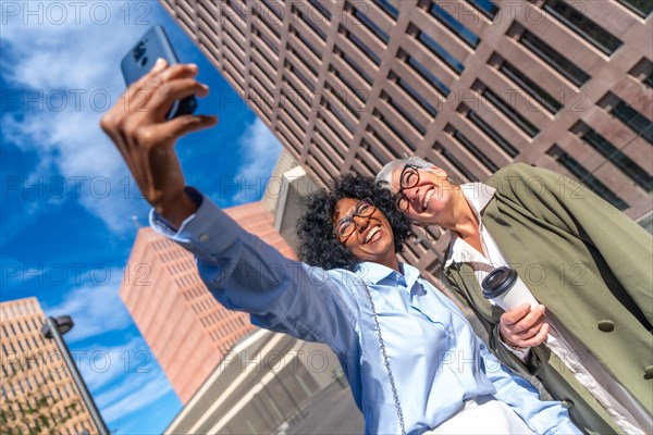 Dynamic low angle view photo of multicultural businesswomen taking a selfie smiling at camera outdoors