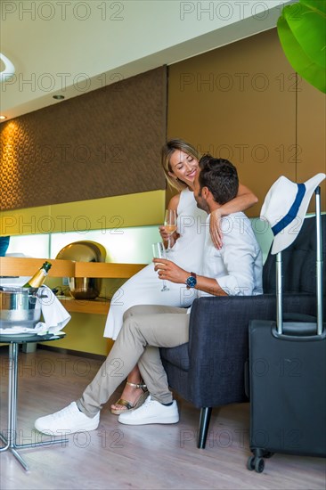Vertical photo of lovers drinking champagne in an hotel room upon arrival with luggage next to them