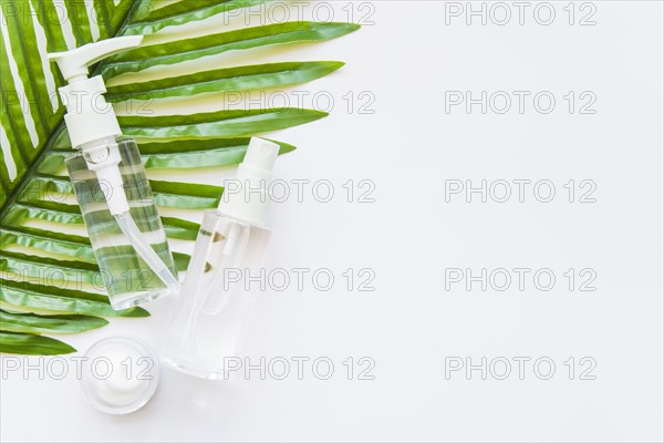 Two transparent cosmetic bottle with spray head moisturizer green leaf against whit e background