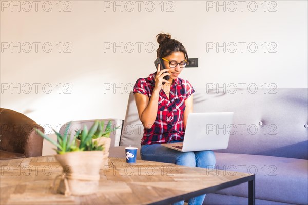Woman using phone while working on remote using laptop sitting on a sofa
