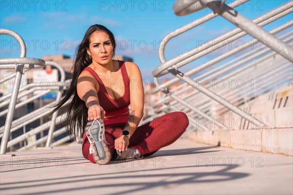 Frontal view of a strong woman sitting on a park stretching the leg