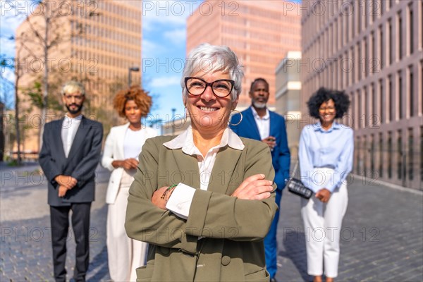 Frontal close-up photo of a mature smiling businesswoman standing proud next to colleagues