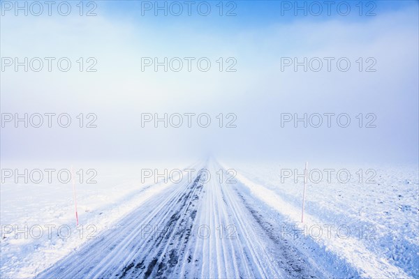 Snowy country road that goes straight into the fog on a cold winter day