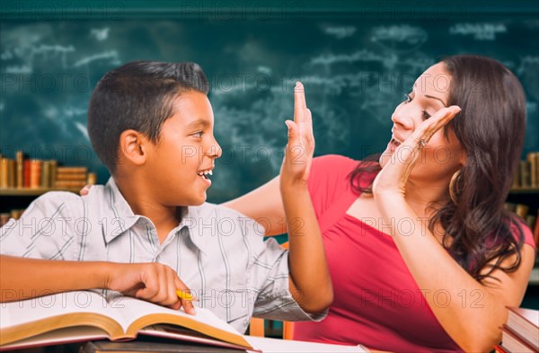 Latina school teacher high fiving a young hispanic boy in the classroom