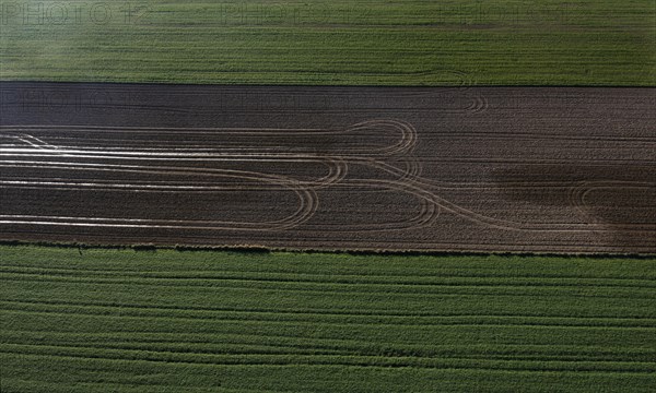 Drone view of green and ploughed fields with tyre tracks