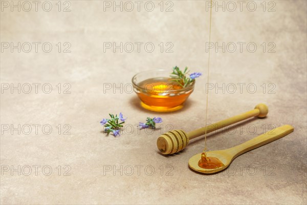 Natural rosemary honey dripping on a wooden spoon with rosemary blossom branches and a bowl with honey