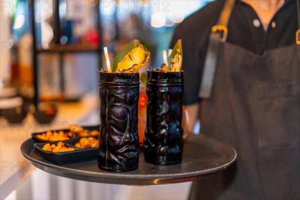 Bartender serving two cocktails in dark glasses in a plate in a night bar