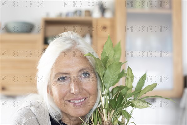 Elderly woman with long hair snuggles up to houseplant at home