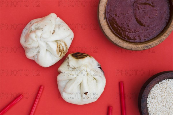 Overhead view dumplings chopsticks sesame seeds sauces red backdrop