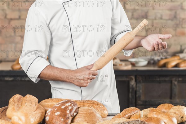 Close up male baker standing table holding rolling pin