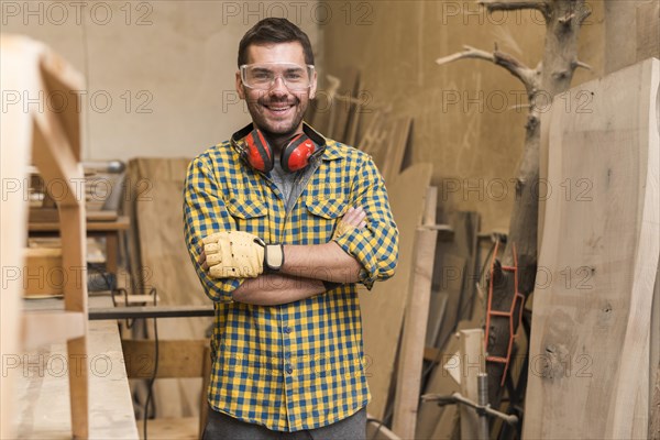 Confident happy carpenter with his arm crossed standing workshop