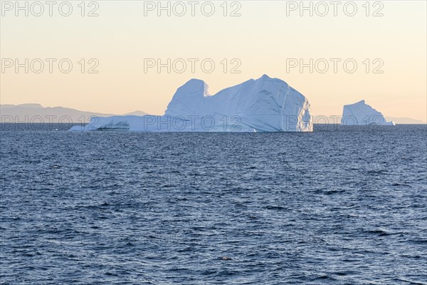 Two icebergs swim in the rising morning sun off the mountains of the Greenland coast. Disko Bay