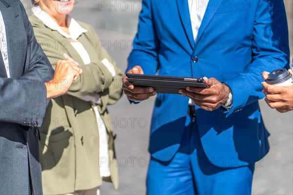 Close-up of the hands of a businessman using digital tablet outdoors surrounded by other business people