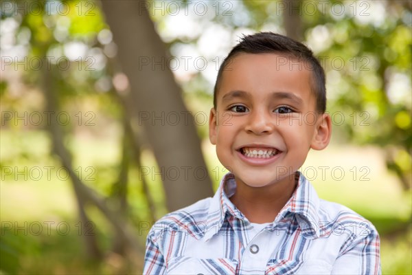 Smiling young hispanic boy outdoors amongst the trees