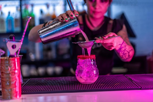 Shaker strains the ingredients into a cocktail glass in the counter of bar at night