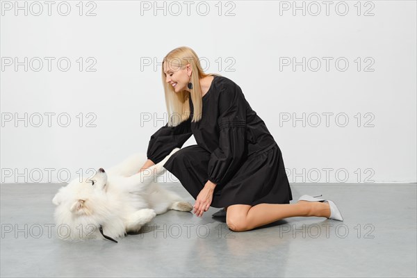 Lovely woman playing with samoyed dog on floor in bright room