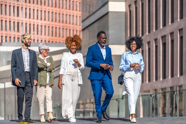 Multicultural business people walking and talking in the city street next to some financial buildings