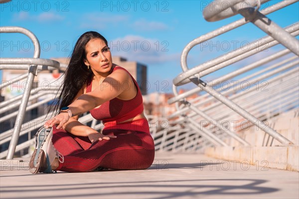 Frontal view of a beauty sportive woman sitting on a park stretching the leg