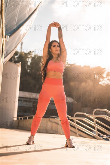 Vertical photo of an athletic woman raising arms to stretch in an urban park