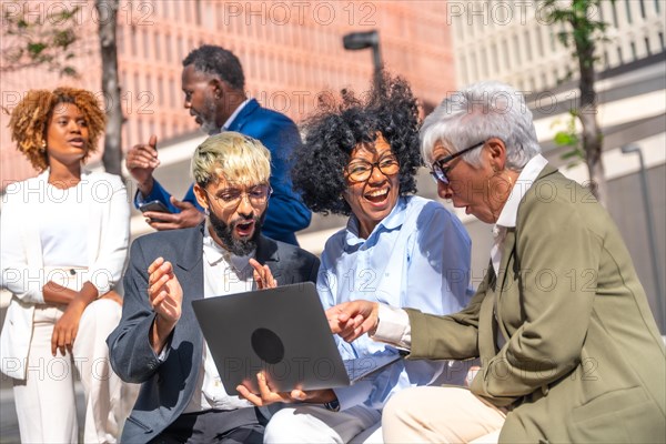 Multi-ethnic group of business people using laptop and celebrating news outdoors