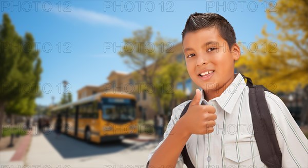 Excited young hispanic boy wearing a backpack giving two thumbs up on campus