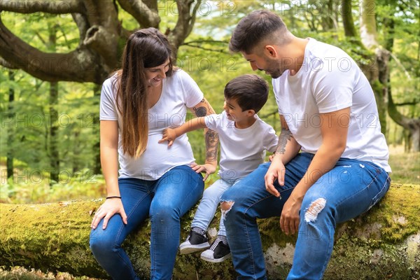 Little boy touching the belly of his pregnant mother sitting on a forest