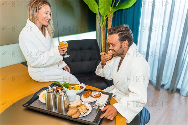 Couple in bathrobe enjoying delicious breakfast in a luxury hotel room