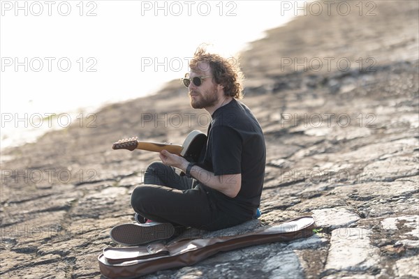 An alone man hipster playing guitar at the quay. Mid shot