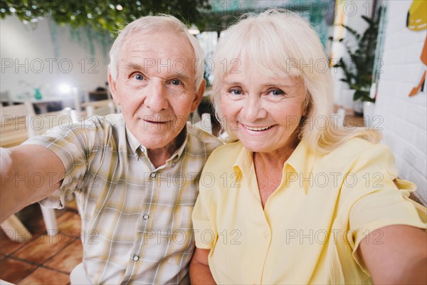 Delighted senior couple hugging sitting cafe shooting selfie