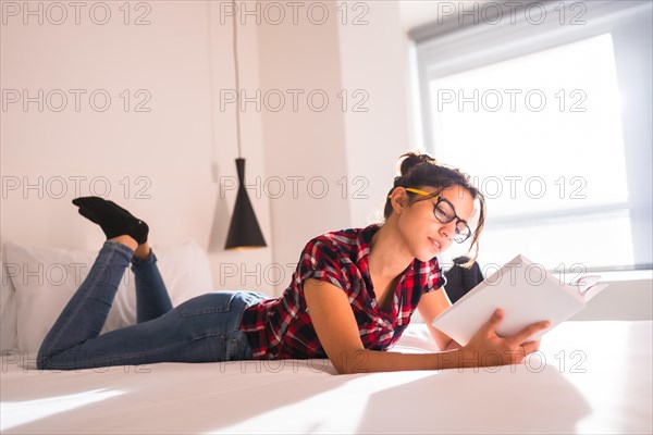 Side view of a beauty young woman lying on a hotel bed reading a book