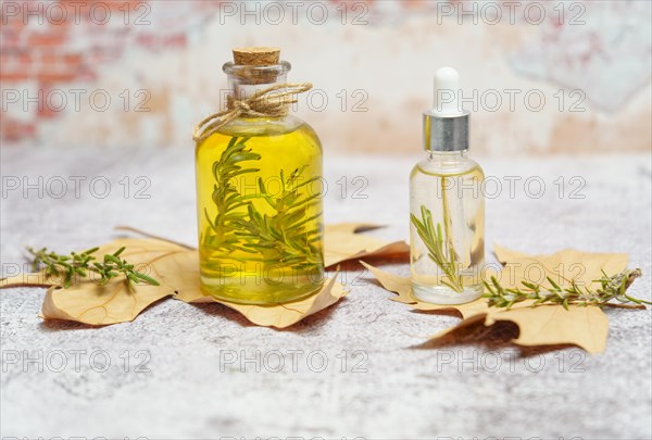 Bottle of rosemary essential oil with fresh branches inside and dropper with oil ready for use on dry leaves