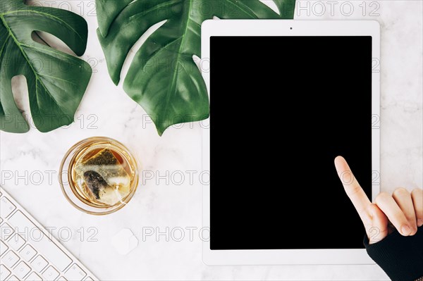 Close up person pointing finger digital tablet with tea glass marble textured backdrop