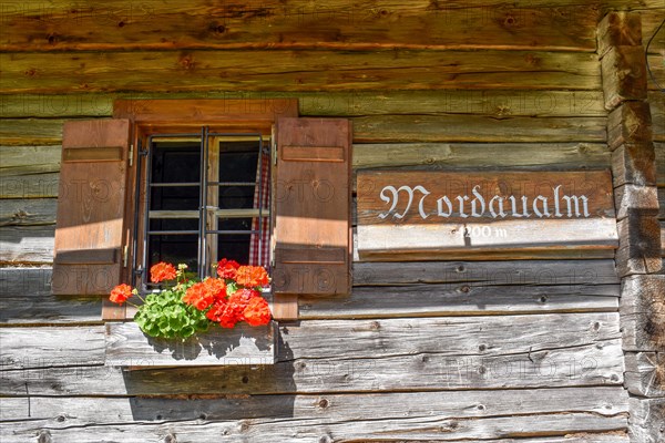 Window of the Mordaualm alpine hut with shutters and geraniums