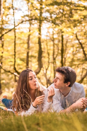 Vertical photo of a playful couple lying together in the forest