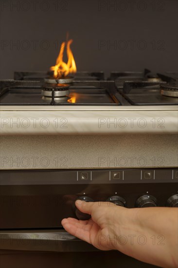 Woman's hand turning on the gas on her kitchen stove energy cost concept