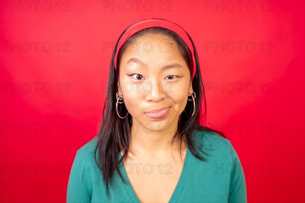 Studio photo with red background of a Chinese woman making funny faces to the camera