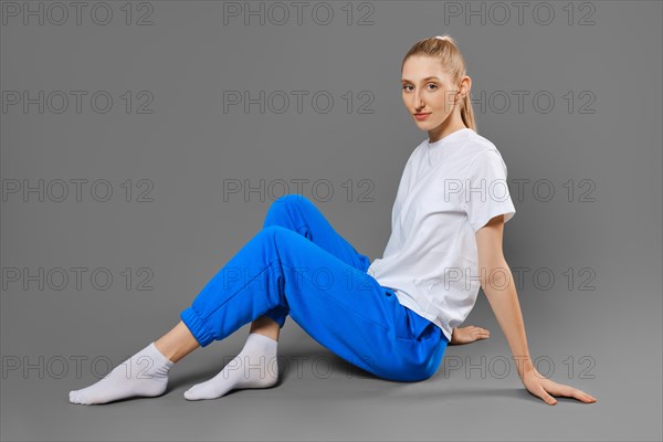 Cute sportive woman sitting on the floor on solid grey background