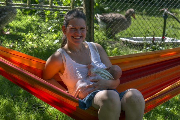 Young mother with baby in a hammock in the garden