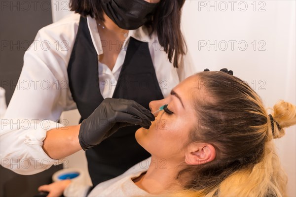 Close-up photo of an unrecognizable professional makeup artist wearing face mask applying false eyelashes to a client