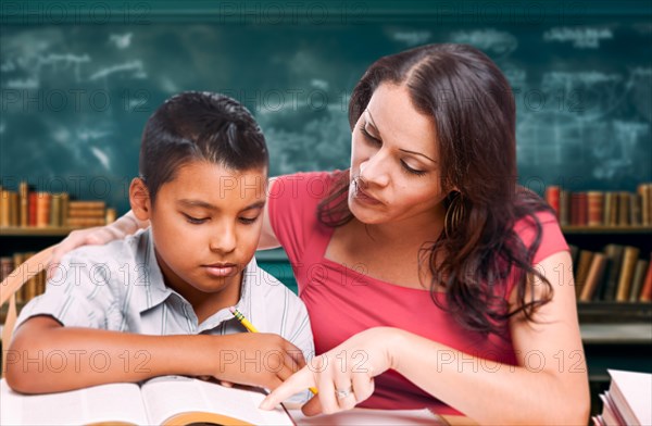 Latina school teacher tutoring a young hispanic boy in the classroom library