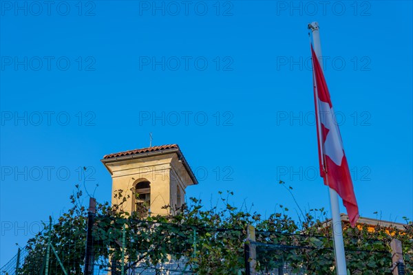 Beautiful Small Church Tower from Medieval and Swiss Flag and Vineplants Against Blue Clear Sky in a Sunny Day in Castello