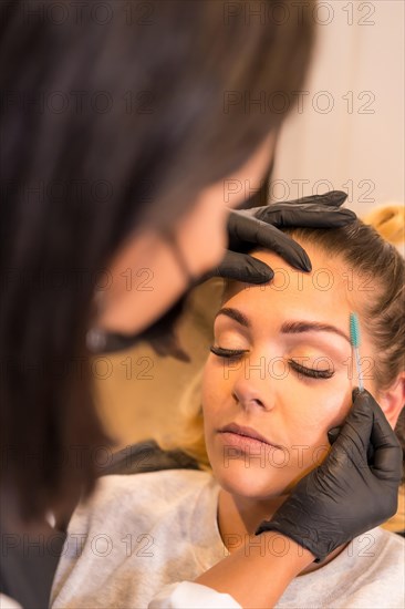 Vertical close-up photo of the rear view of a Hairdresser combing the eyebrows of a client