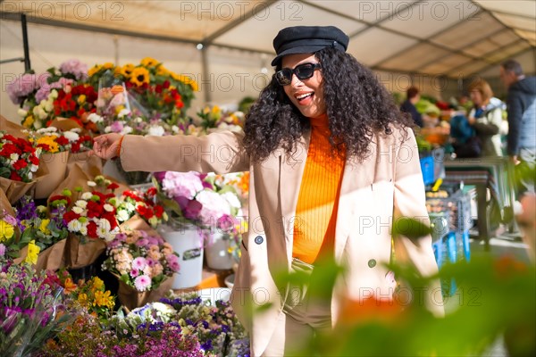 Happy latin woman choosing flowers in an outdoor flower shop in a street market in a sunny day of winter