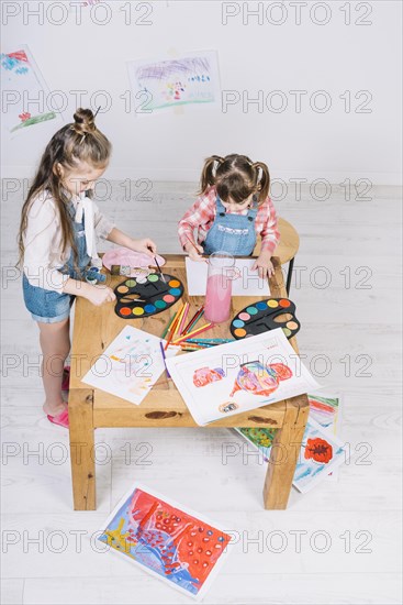 Two little girls painting with aquarelle paper table