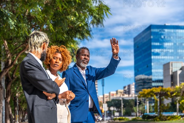 Multi-ethnic business people waiting for a cab and an african mature businessman gesturing to stop one in the city