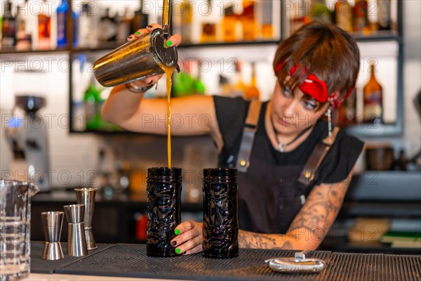 Alternative young bartender pouring cocktail into a creative glass in the counter of a bar