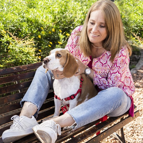 Portrait of beautiful woman sitting on wooden bench with her beagle dog