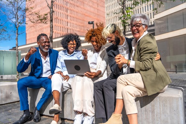 Happy group of multi-ethnic business people using laptop sitting on a bench outdoors