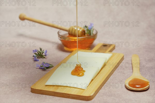 Drizzle of honey dripping on cheese slices with fresh rosemary branches in bloom and a glass bowl with rosemary honey