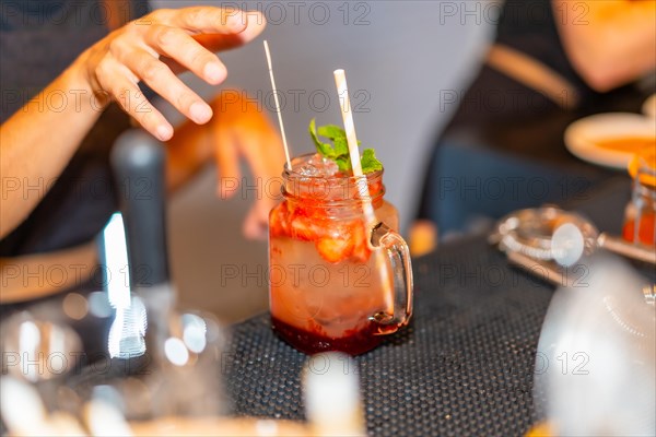 Close-up of a red mezcal margarita cocktail garnished with mint in the counter of a bar while bartender preparing it